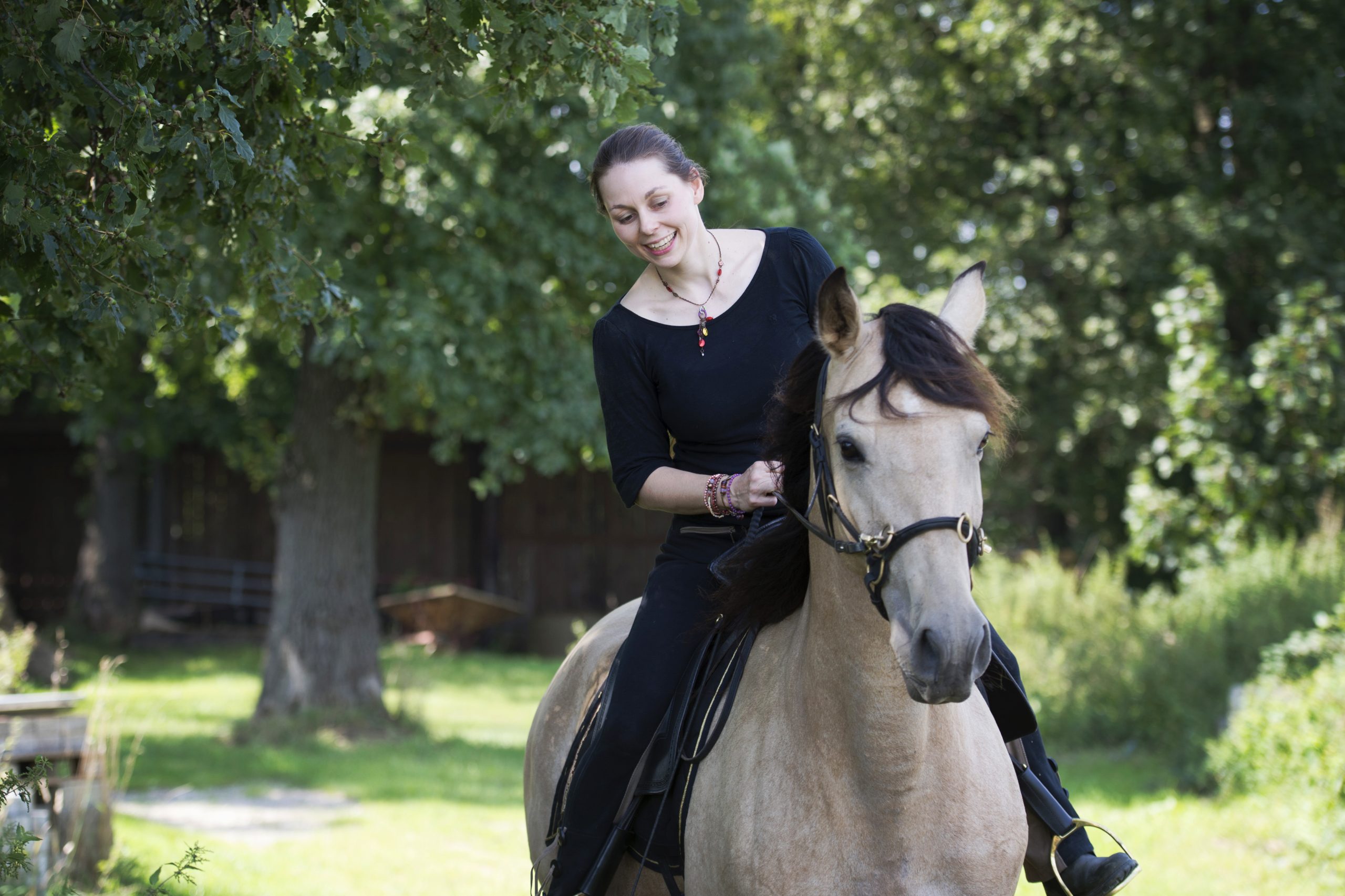 Reiterin sitzt auf einem hellen Pferd und blickt während des Reitens nach unten.
